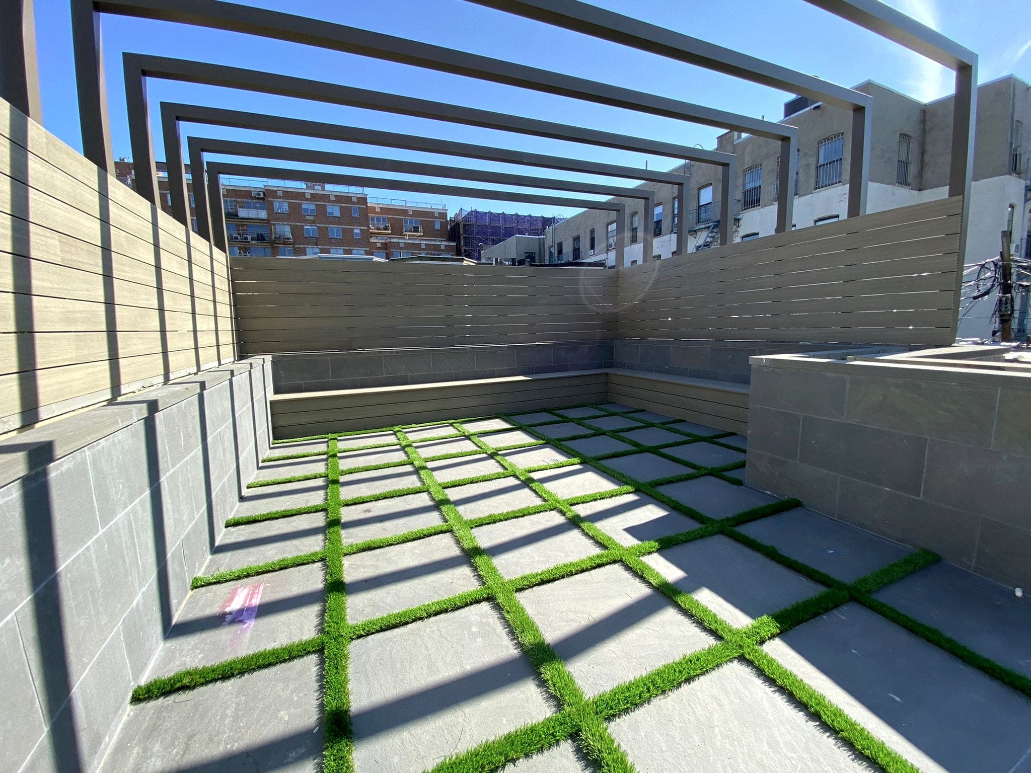 Rooftop with paver-and-grass grid floor and a black steel pergola frame